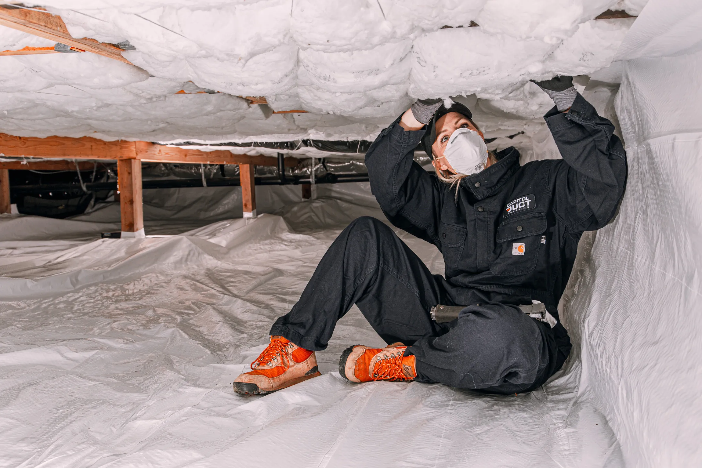 Crawl space technician in protective gear inspecting insulation in a crawl space in Lacey, WA.