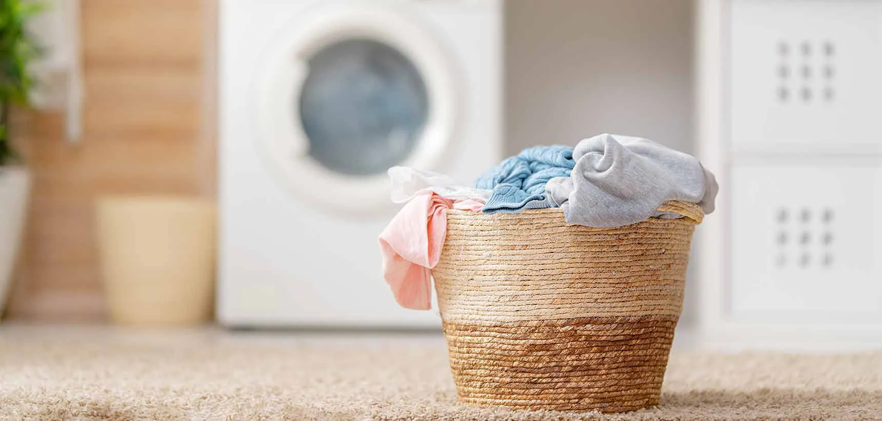 Laundry basket full of clothing in front of a washer and dryer.