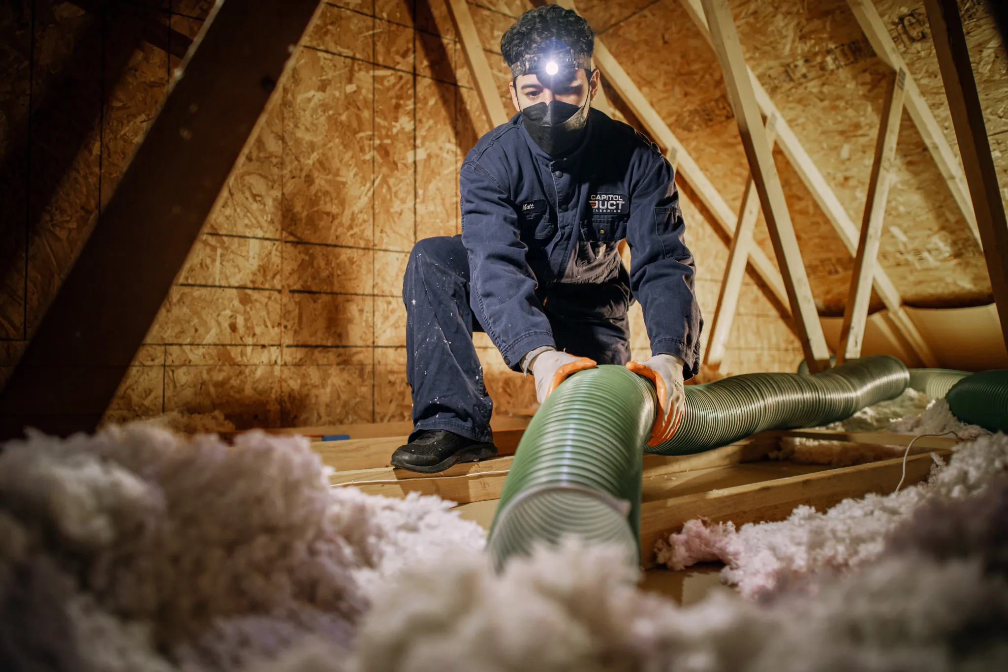 Technician in protective gear sealing a crawl space support beam with insulation tape in Auburn, WA.